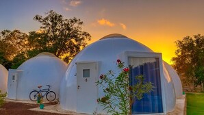 En række kuppelformede yurts med en cykel parkeret foran en af dem, foran en solnedgang.