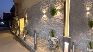 A building facade with a textured stone wall, potted plants, and illuminated wall sconces. - Rizk Pyramids View Hotel (Giza)