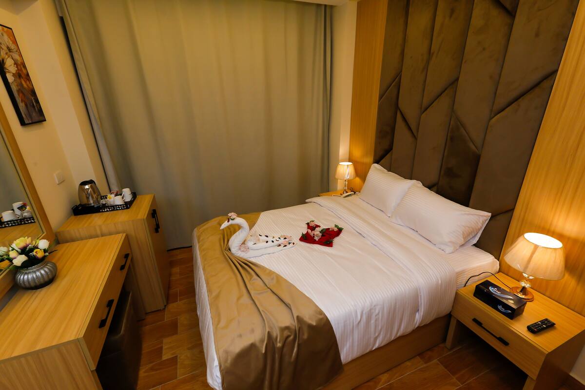Una habitación de hotel con cama, mesita de noche y escritorio con lámpara.