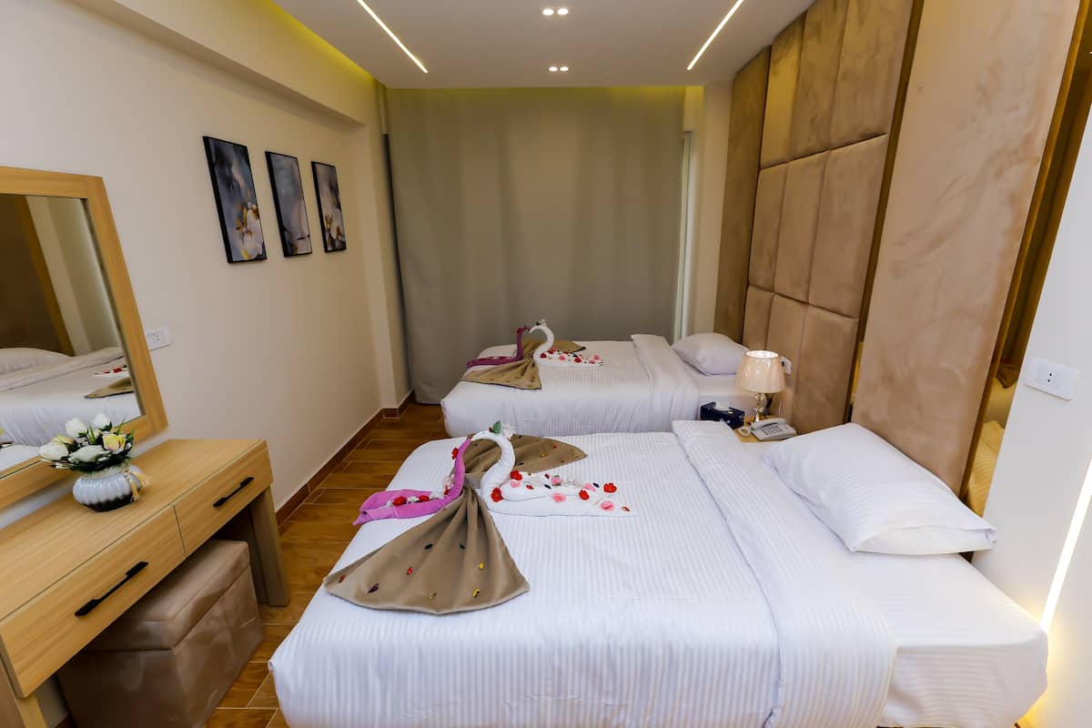 Una habitación de hotel con dos camas, un escritorio de madera, un espejo y obras de arte en la pared.