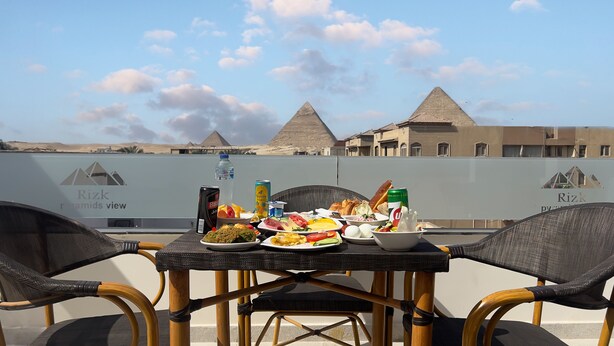 A dining table with a variety of food items and drinks, set against a backdrop of the pyramids and a clear sky. - Rizk Pyramids View Hotel (Giza)