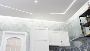 A modern kitchen with white cabinets, a marble backsplash, and recessed ceiling lighting.