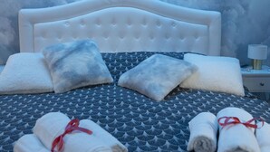 A bed with a patterned bedspread, two pillows, and rolled towels tied with red ribbons.