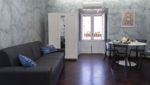 A modern living room with a dark sofa, a dining table with chairs, and a white wardrobe.
