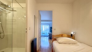 Une petite pièce avec une cabine de douche en verre, un lit avec une tête de lit en bois et une lampe de chevet.