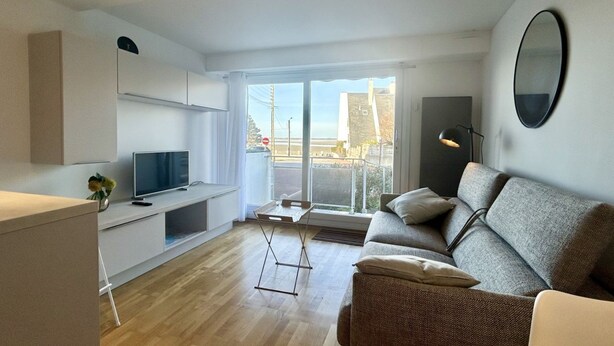 Un salon moderne avec un canapé, un téléviseur, une petite table et un balcon offrant une vue agréable.