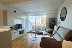 Una sala de estar moderna con un sofá, un televisor, una mesita y un balcón con vistas.