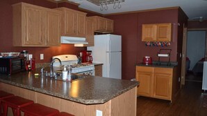 A kitchen with wooden cabinets, a granite countertop, a stove, a refrigerator, and a microwave. There are red bar stools and a ceiling light fixture. - Cozy home in the heart of the Allagash.  Great for fishing, hiking, hunting, ect (Allagash)