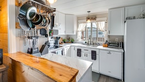 Cocina con alacenas blancas, encimera de madera, un colgador para ollas y un letrero que dice 'Kitchen'.