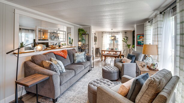 Una sala de estar moderna con un sofá gris, un reposapiés y un sillón, una mesita de madera y un comedor con mesa y sillas.