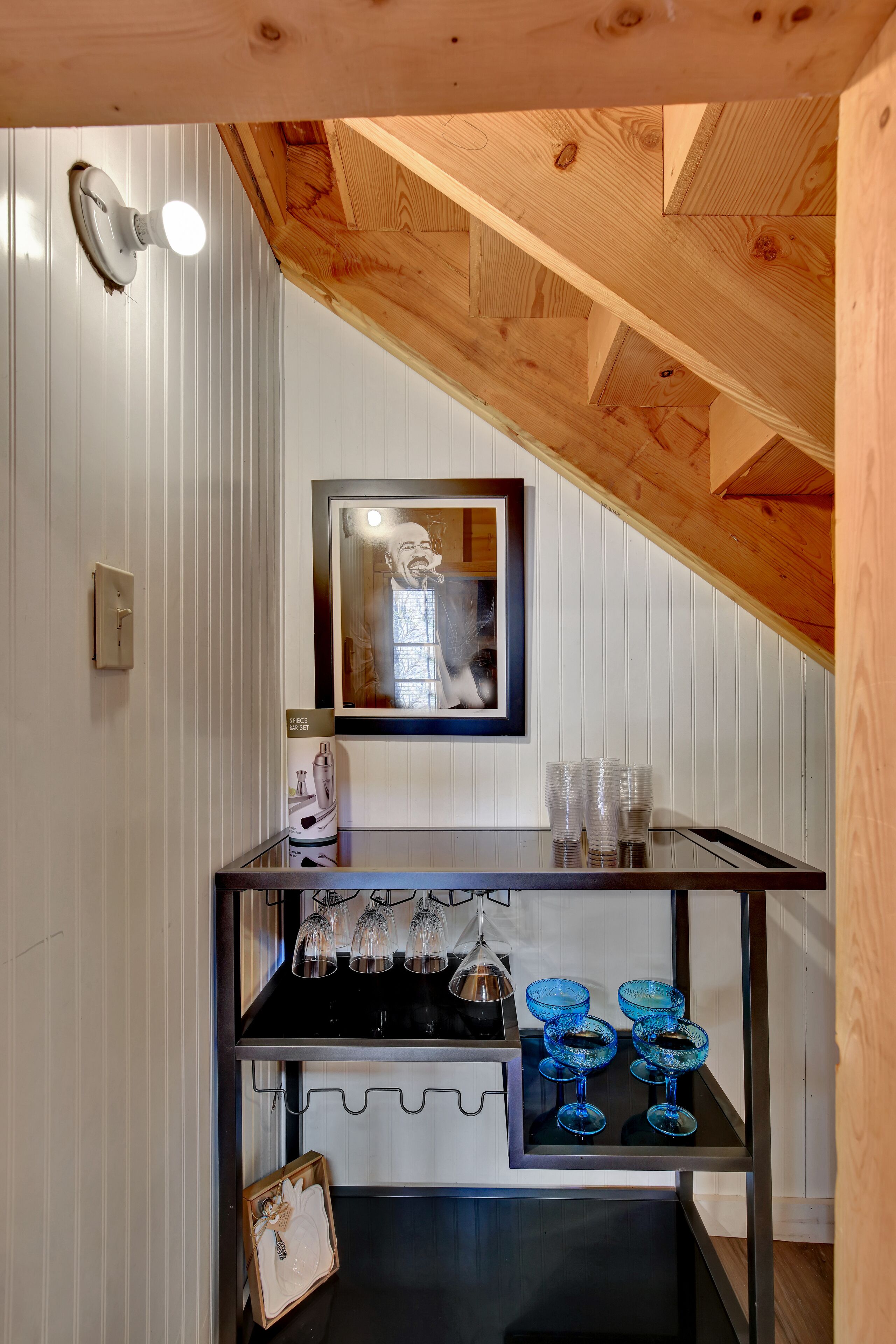 Une cuisine avec des poutres en bois, un tableau encadré au mur, un plan de travail noir avec de la verrerie et un luminaire suspendu.