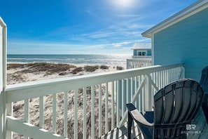 A beach view from a balcony with a white railing, a small building, and a chair.