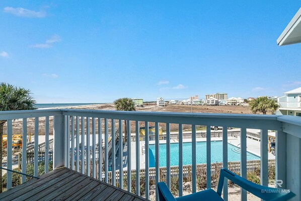 A wooden deck with a white railing overlooking a swimming pool and a view of buildings in the distance.