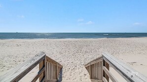 A wooden boardwalk leading to a sandy beach with a clear blue sky.