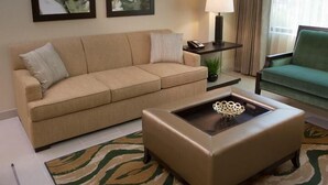 A living room with a beige sofa, a small table with a lamp, a green armchair, and abstract art on the wall. - The Berkley (Las Vegas)