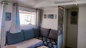 Una habitación acogedora con sofá, ventana con cortinas, aire acondicionado y un reloj de pared.