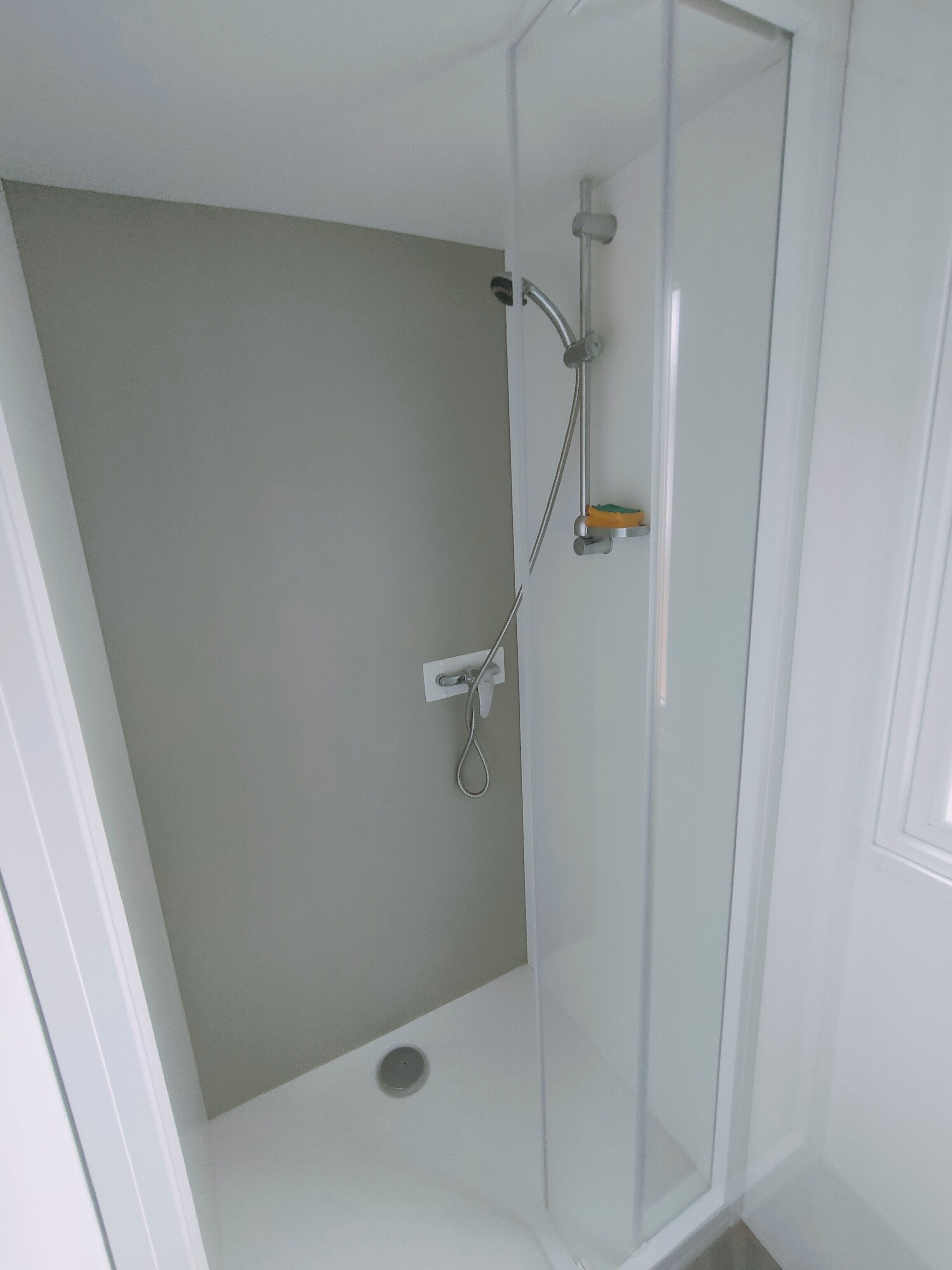 Un área de ducha pequeña y cerrada con puerta de cristal, un cabezal de ducha manual y un grifo de pared.
