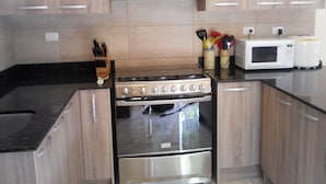 A kitchen with a stainless steel stove, a microwave, and a toaster. There are wooden cabinets and a black countertop. - Beachfront Nature Rentals. Private Ground Floor Studio in Guesthouse (Quebro, District of Mariato)