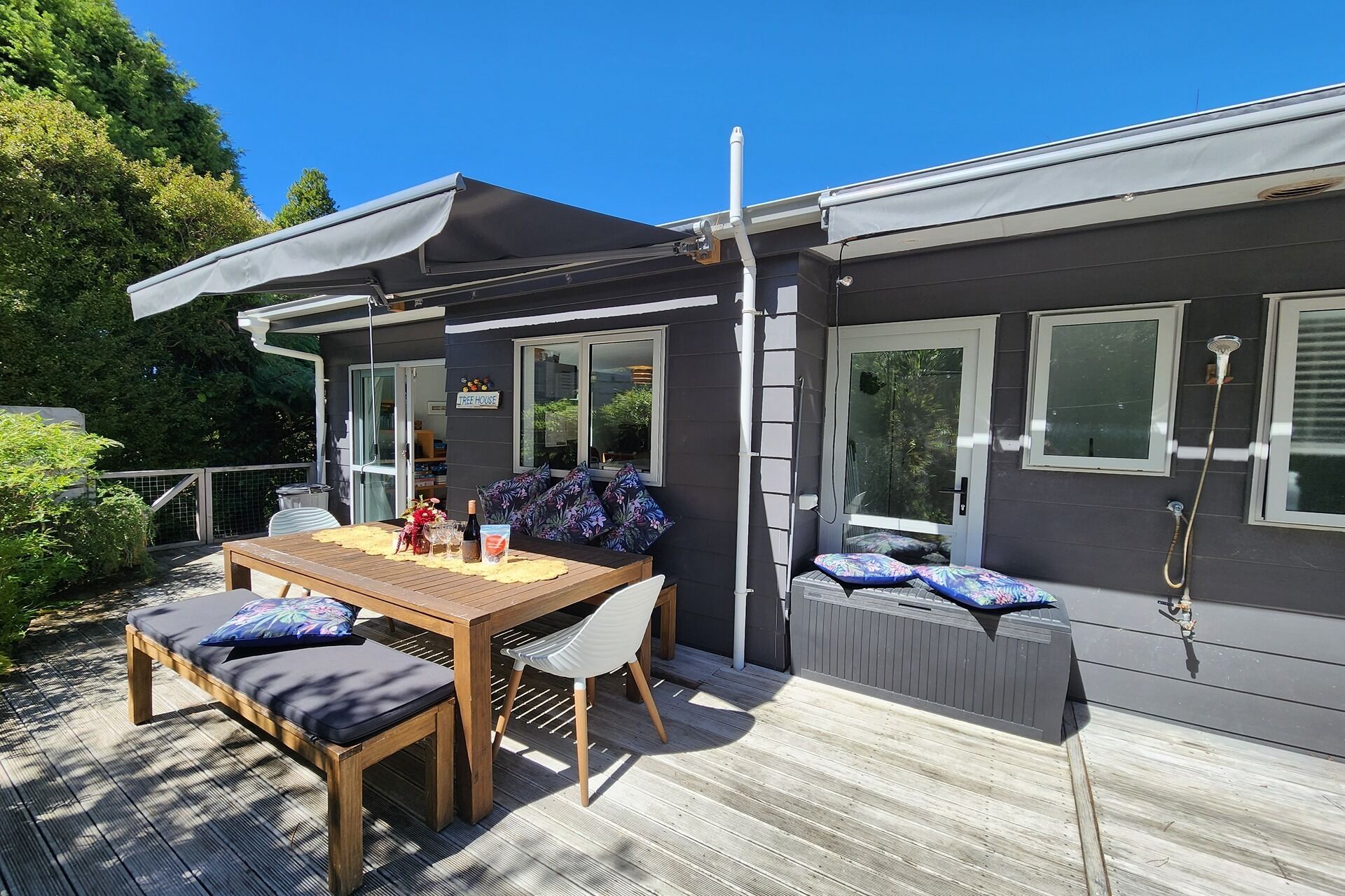 Ein modernes Haus mit einer Terrasse, einem Essbereich mit Tisch und Stühlen sowie einer überdachten Sitzgruppe mit Kissen.