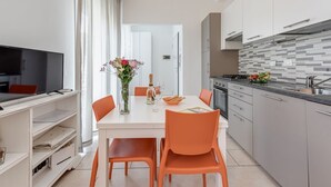 A modern kitchen with grey cabinets, a white countertop, and a dining area with a table and orange chairs.