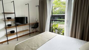A bedroom with a bed, a TV on a shelf, a desk, and a view of greenery outside.