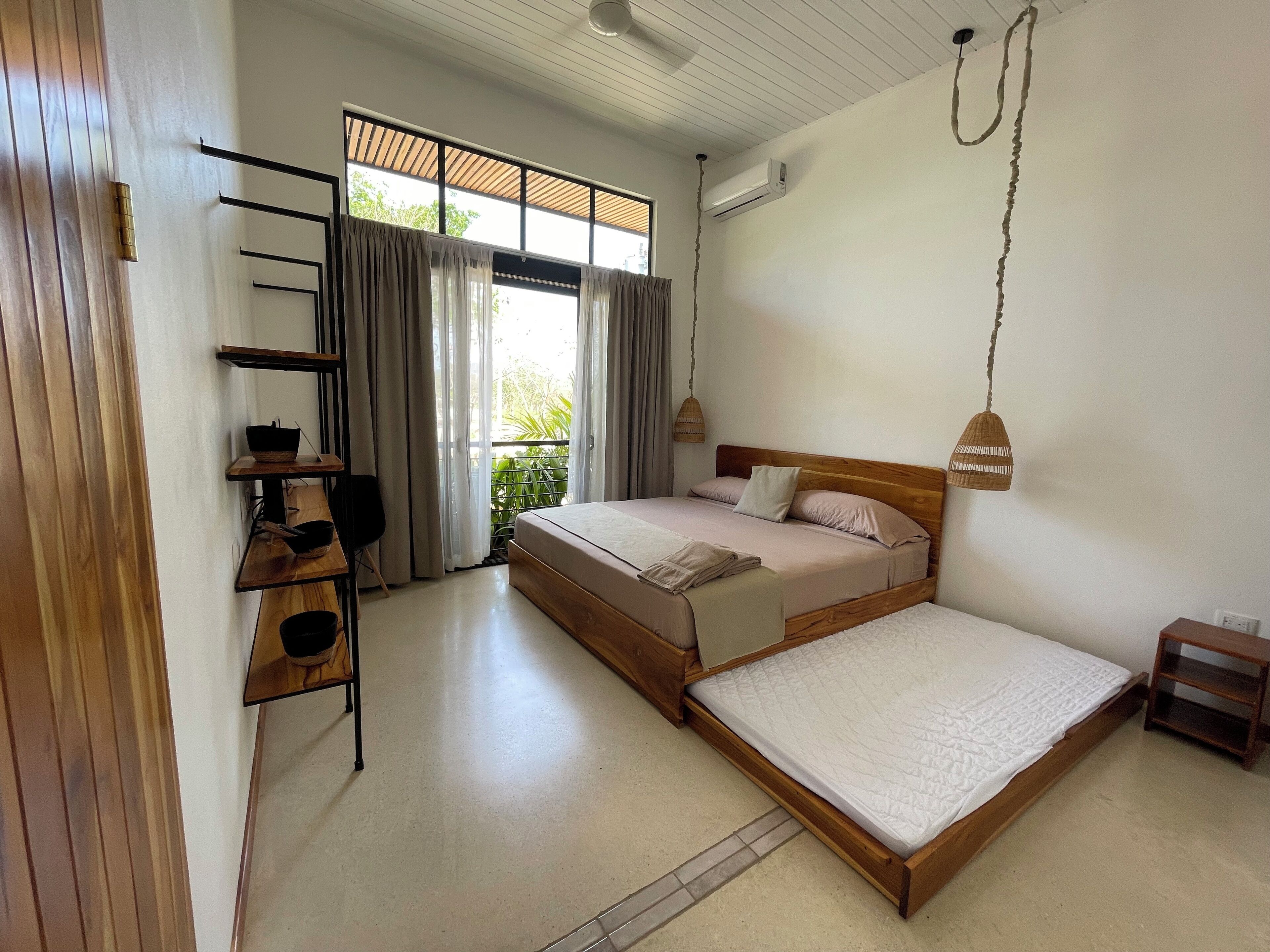 A bedroom with a large bed, a wooden desk, and a window with curtains.