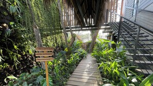 A wooden pathway leading to a hotel entrance, surrounded by lush greenery and a metal staircase. - Mar Botánico - Avellanas Beach Hotel (Veintisiete de Abril)