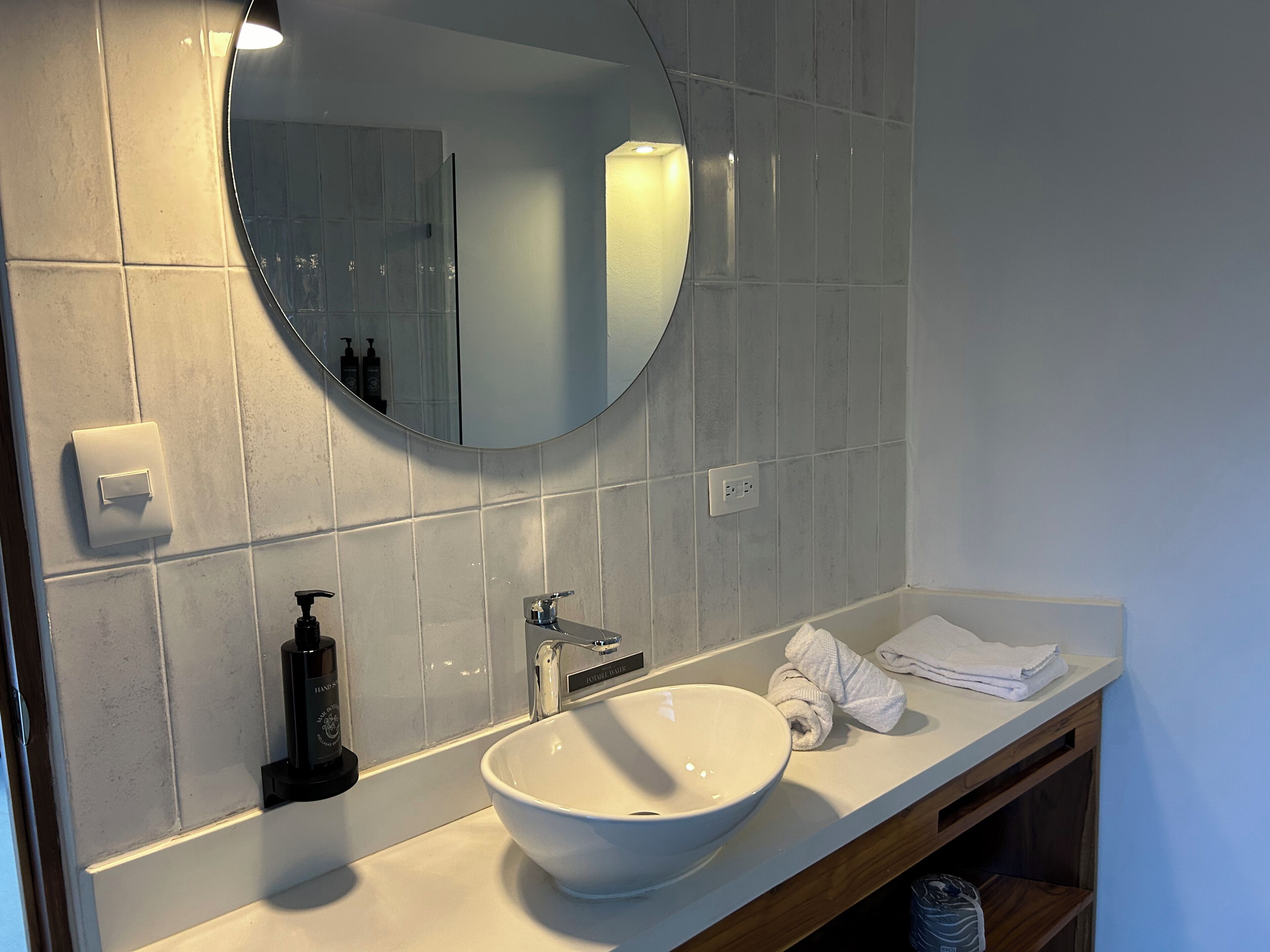 A modern bathroom with a white sink, a round mirror, and a towel rack.