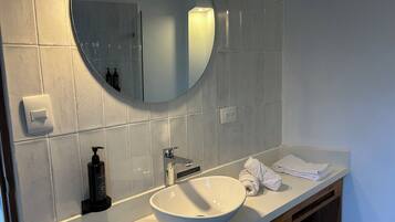 A modern bathroom with a white sink, a round mirror, and a towel rack.