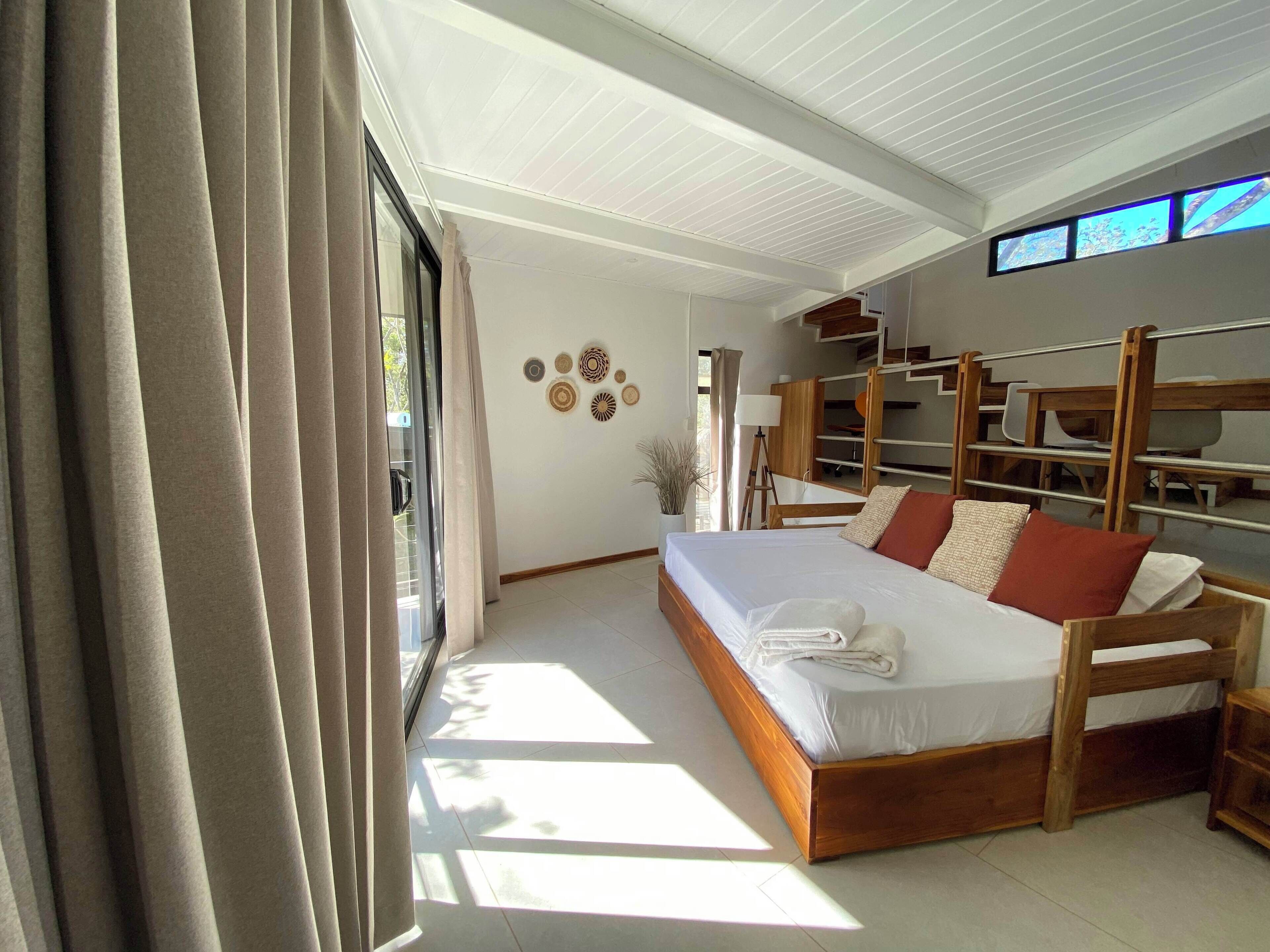 Ein Schlafzimmer mit einem großen Bett, Holzbettstühlen, einem Schreibtisch und einem Fenster mit Vorhängen.