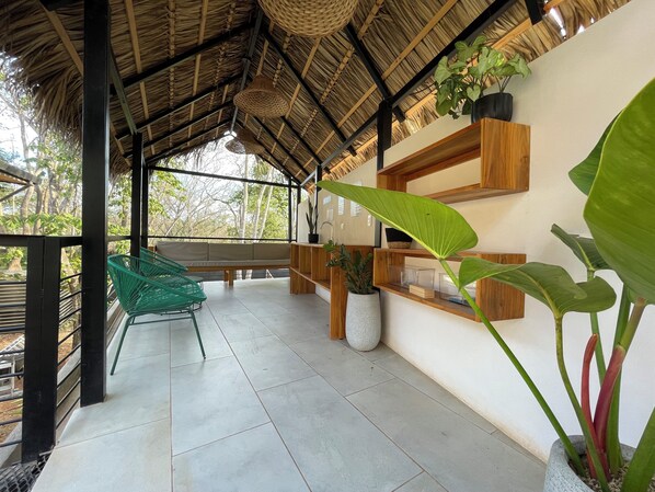 A covered outdoor seating area with a thatched roof, wooden shelves, and potted plants. - Mar Botánico - Avellanas Beach Hotel (Veintisiete de Abril)