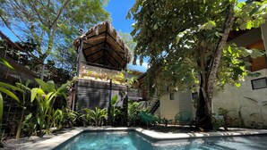 A swimming pool with a thatched-roof structure and green chairs nearby. - Mar Botánico - Avellanas Beach Hotel (Veintisiete de Abril)