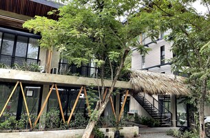 A modern building with a staircase, a thatched roof structure, and surrounding greenery.