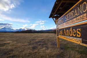 A sign for Camping Serrano with a view of mountains in the background.
