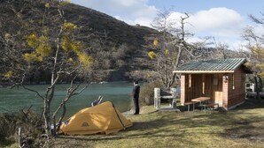 Un terrain de camping avec une tente, une petite cabane en bois, une table et un banc.