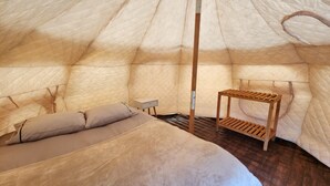 Un intérieur chaleureux, aménagé comme une tente, avec un lit, une petite table et un banc en bois.