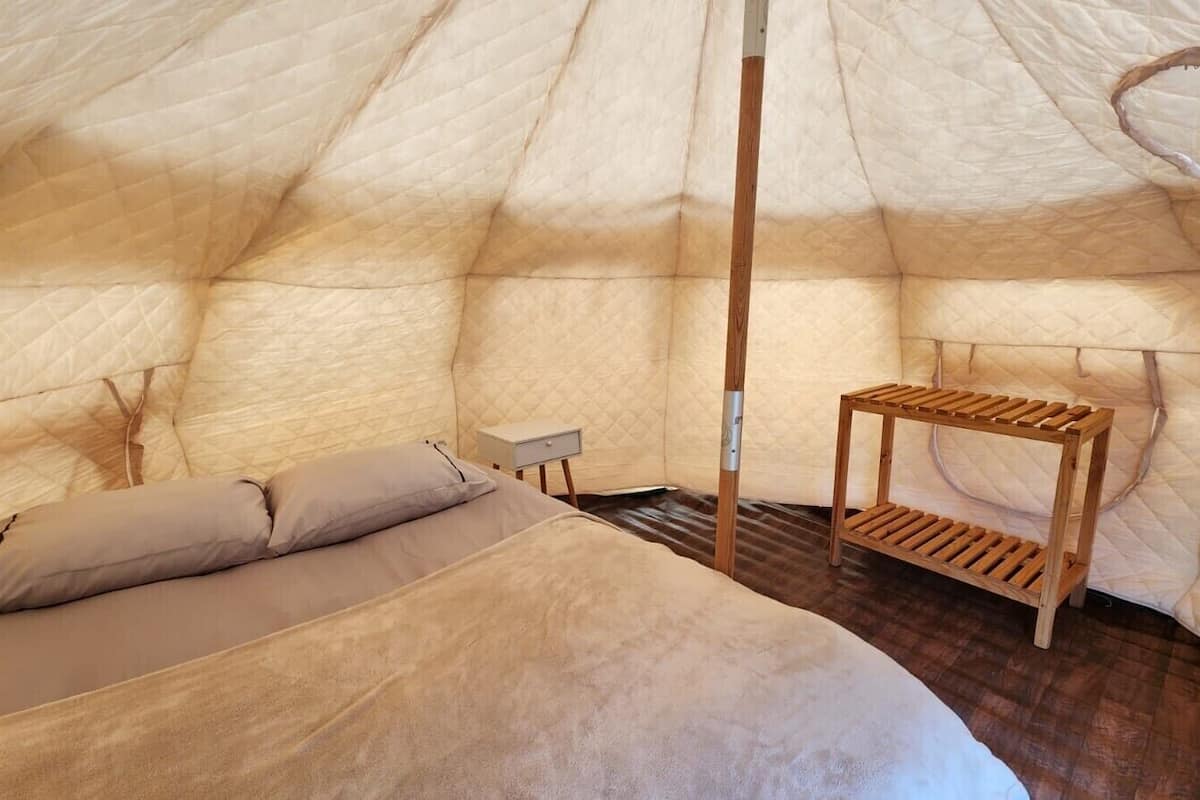 Un interior acogedor de un alojamiento tipo tienda de campaña, con una cama, una mesita y un banco de madera.