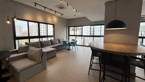 A modern living room with a sofa, chairs, a dining table, and large windows offering city views. - Studio em Perdizes - em frente a PUC (São Paulo)
