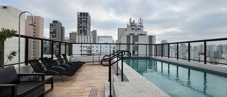 A rooftop pool area with lounge chairs and a view of the city skyline.