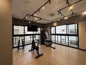 Ein modernes Fitnessstudio mit großen Fenstern, Deckenleuchten und unterschiedlichen Trainingsgeräten.