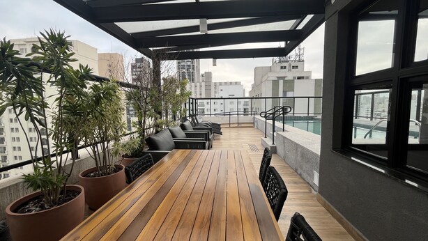 A rooftop terrace with wooden flooring, black outdoor furniture, and potted plants. - Studio em Perdizes - em frente a PUC (São Paulo)