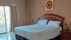 A bedroom with a bed, a nightstand, a ceiling fan, a window with curtains, and a wall with a flower painting. - Amplia Casa Para Renta Vacacional en Mazatlán a Solo 6 Minutos de la Playa (Mazatlán)