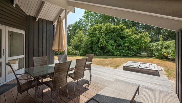 An outdoor patio with a glass table and wicker chairs, a covered area with a beige umbrella, and a view of a wooded backyard. - Gorgeous home in Sydals with WiFi (Sydals)