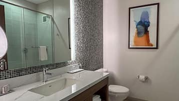 Une salle de bain avec un grand miroir, un lavabo, des toilettes et un tableau abstrait encadré accroché au mur.
