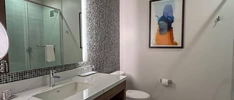 Un baño con un espejo grande, un lavabo, un inodoro y un cuadro abstracto enmarcado en la pared.