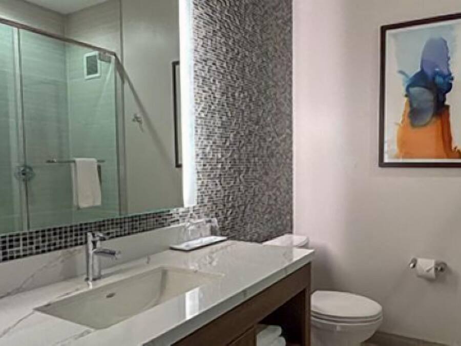 Une salle de bain avec un grand miroir, un lavabo, des toilettes et un tableau abstrait encadré accroché au mur.