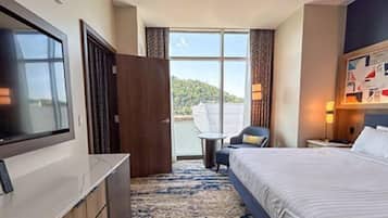 A hotel room with a large bed, a television, a desk, and a view of the outdoors.
