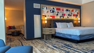A modern hotel room with a large bed, a desk, a sofa, and a patterned carpet.