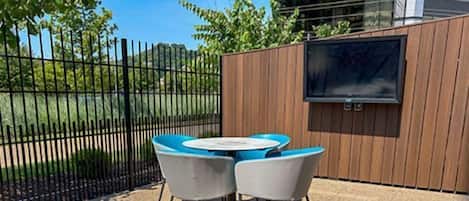 An outdoor seating area with a table and chairs, a wooden fence, and a television mounted on the wall.