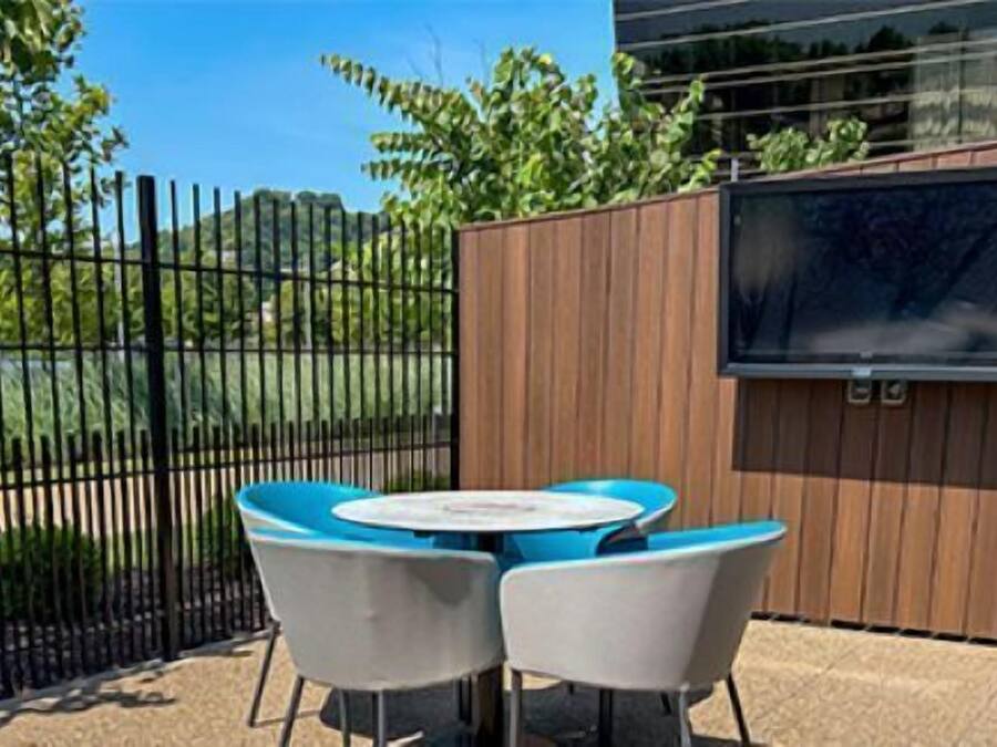 Un espacio al aire libre con mesas y sillas, cerca de una valla de madera, y un televisor fijado a la pared.